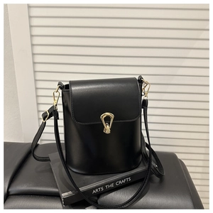 Detail of matte black bucket bag showing a stylish gold-tone metal buckle and texture
