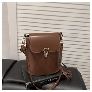 Detail of warm brown bucket bag showing the unique gold metal lock and smooth PU leather
