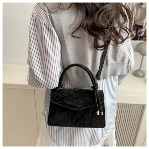 Détail d'un sac bandoulière noir à texture froncée et finitions métalliques dorées