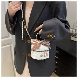 Detail of white quilted mini bucket bag with gold flower charm and elegant ribbon