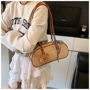 Detail of straw woven cylindrical shoulder bag with leather trim and bear pendant
