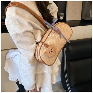 Close-up of woven straw shoulder bag with leather trim and cute teddy bear charm