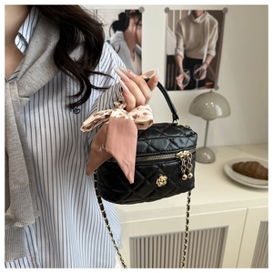 Detail of black quilted crossbody bag with gold floral accent and decorative silk scarf