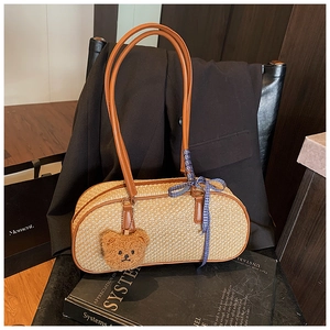 Detail of woven straw shoulder bag with brown leather handles and a plush bear charm