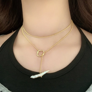 Close-up of double-layer golden necklace featuring a white baroque pearl and ring pendant