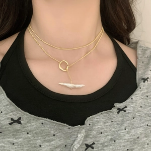 Close-up of double-layered gold necklace featuring a baroque pearl and metal ring pendant