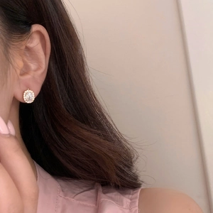 Close-up of rose gold oval stud earring with central gemstone and crystal pavé on ear