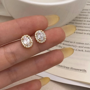 Close-up of gold halo stud earrings with oval zircon center stone held by hand