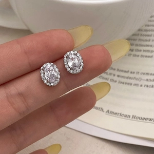 Macro shot of silver oval zircon stud earrings with crystal halo detail held by hand