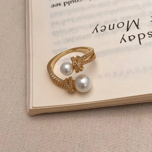 Détail de la bague dorée ouverte avec doubles perles et nœud en zircon sur un livre
