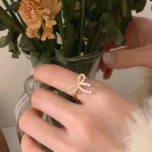 Close-up of golden bow ring with white pearls and sparkling zircons on finger
