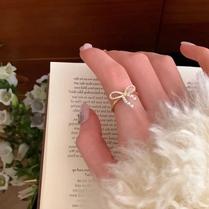 Detailed view of golden bow ring featuring a white pearl and shimmering zircon stones