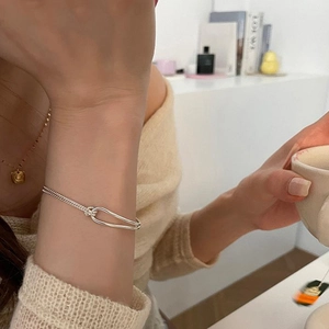 Silver double-strand knot bracelet on woman wrist with minimalist oval clasp detail