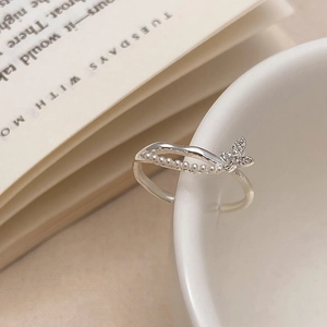 Detail of silver butterfly ring with small pearls and crystals on a white ceramic cup