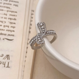 Detailed view of silver bow ring featuring small pearls and zircon stones on white porcelain