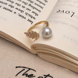 Detail view of gold open ring featuring a sparkling leaf motif and white shell pearl