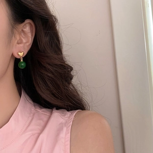 Detail of a woman wearing gold heart stud earrings with green chalcedony bead drops