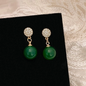 Détail de boucles d'oreilles dorées avec cristaux pavés et perles vert émeraude