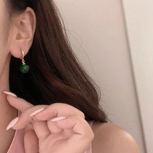 Gros plan de boucles d'oreilles créoles dorées avec pendentif calcédoine verte sur modèle