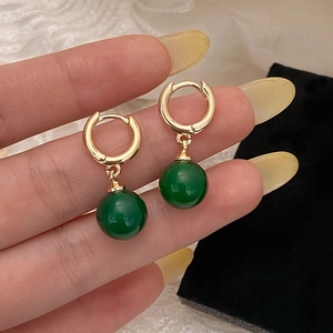 Boucles d'oreilles créoles dorées avec pendentifs en calcédoine verte entre les doigts