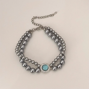 Détail du collier de perles gris foncé à deux rangs avec pierre centrale bleue et fermoir mousqueton