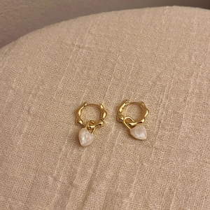 Élégantes boucles d'oreilles créoles dorées avec pendentifs cœurs crème sur fond de lin