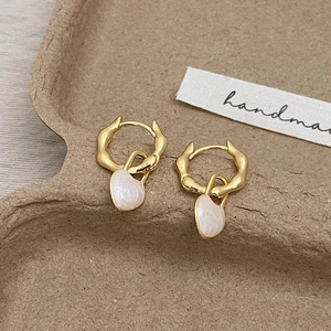 Détail de boucles d'oreilles dorées texture lave avec pendentifs cœur nacré