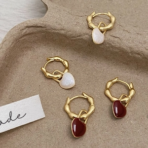 Détail de boucles d'oreilles cœur bordeaux et perles avec anneaux dorés ondulés sur plateau