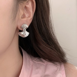Detail of silver hammer-textured fan earrings with white pearl accents worn on model