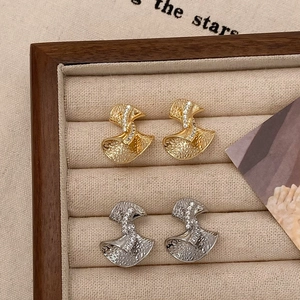 Bow-knot style hammered zircon earrings in gold and silver finish on a jewelry box