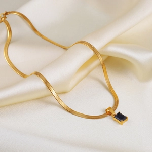Close-up of golden snake chain necklace with rectangular dark blue gemstone on silk