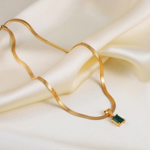 Close-up of gold snake chain with rectangular green gemstone pendant on silk fabric