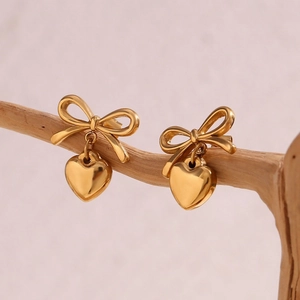 Elegant gold bow and heart dangle earrings on a natural wood branch with soft light