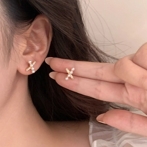 Detail of gold X-shaped earrings with micro-inlaid pearls and small crystals on ear
