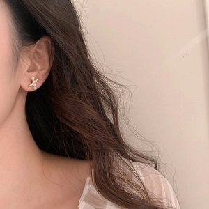 Elegant gold-tone cross stud earrings with delicate pearls shown on a model's ear
