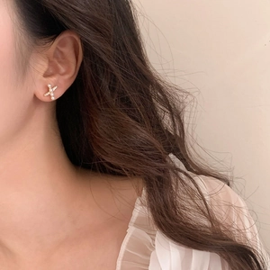 Detail of cross-shaped stud earring with white pearls and rhinestones on ear