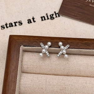 Close-up of X-shaped pearl earrings with cubic zirconia on a beige velvet jewelry box