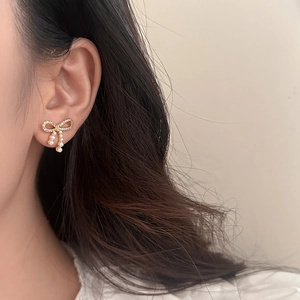 Elegante goldene Schleifenohrringe mit Zirkonia und weißen Perlen am Model getragen