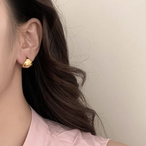 Close-up of a high-polish gold teardrop hoop earring worn by a model on a beige background
