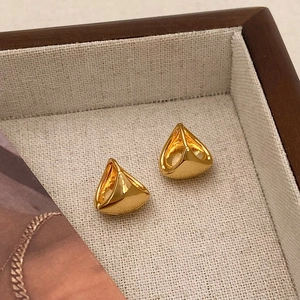 Detailed view of geometric gold hoop earrings with a polished finish in a wooden tray
