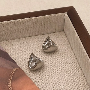 Detailed view of silver triangular pyramid stud earrings on a beige linen display tray