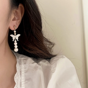 Detail of elegant butterfly pearl earrings with gold tassels on a fashion model