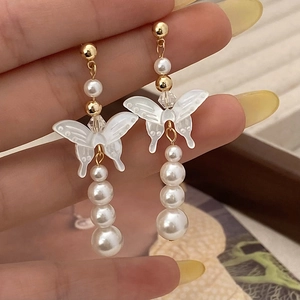 Detail of elegant gold drop earrings featuring white butterfly motif and tiered pearls
