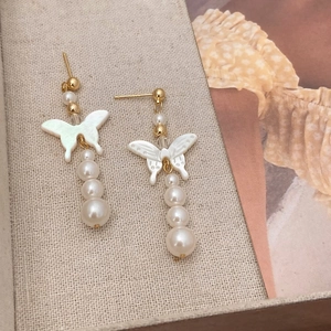 Elegant butterfly drop earrings with natural shell and pearls on a textured fabric