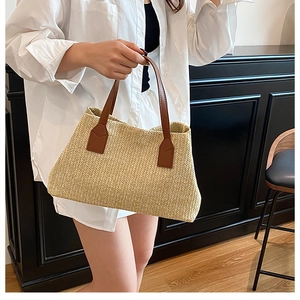 Detail of a beige straw tote bag with brown leather handles on an indoor background