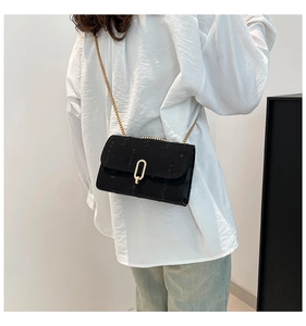 Close-up of black textured fabric bag with polished gold oval hardware and chain strap