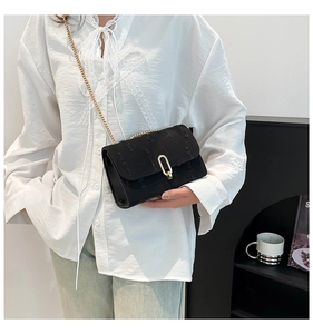 Detail of a black textured crossbody bag with gold chain strap on a white shirt