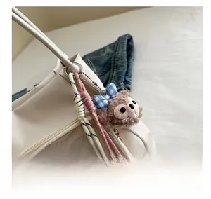 Close-up of brown plush koala charm and colorful braided ropes on messenger bag