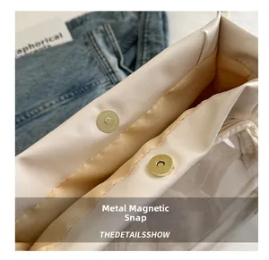 Detail view of the golden magnetic clasp on a cream leather bag with interior PVC layer