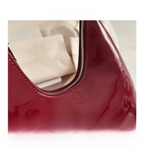 Macro detail of glossy dark red patent leather shoulder bag with embossed branding